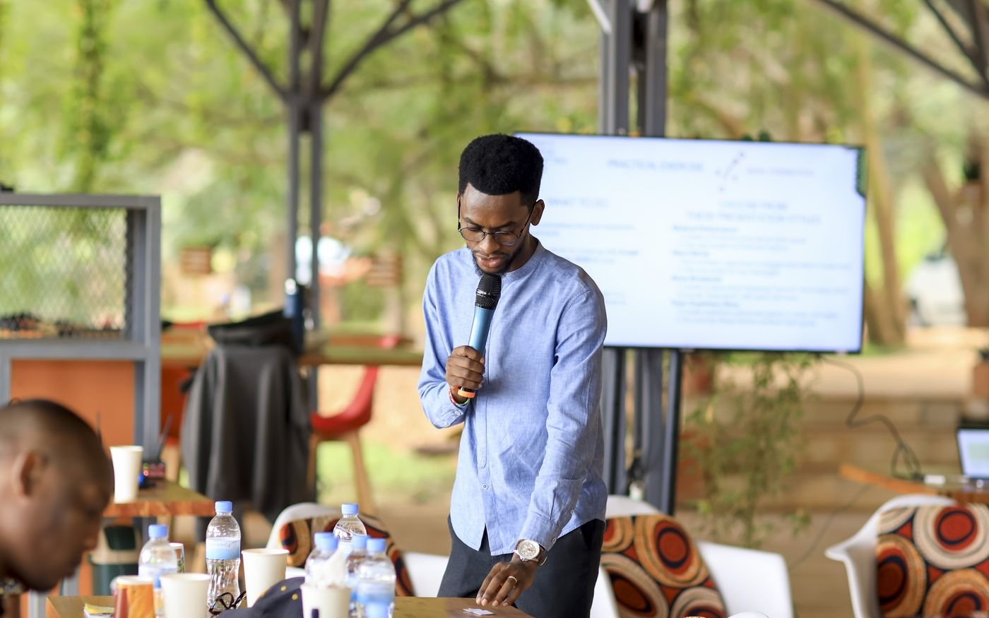 A facilitator speaking into a microphone during an Intego Academy session in Kigali, with participants seated around a long table.